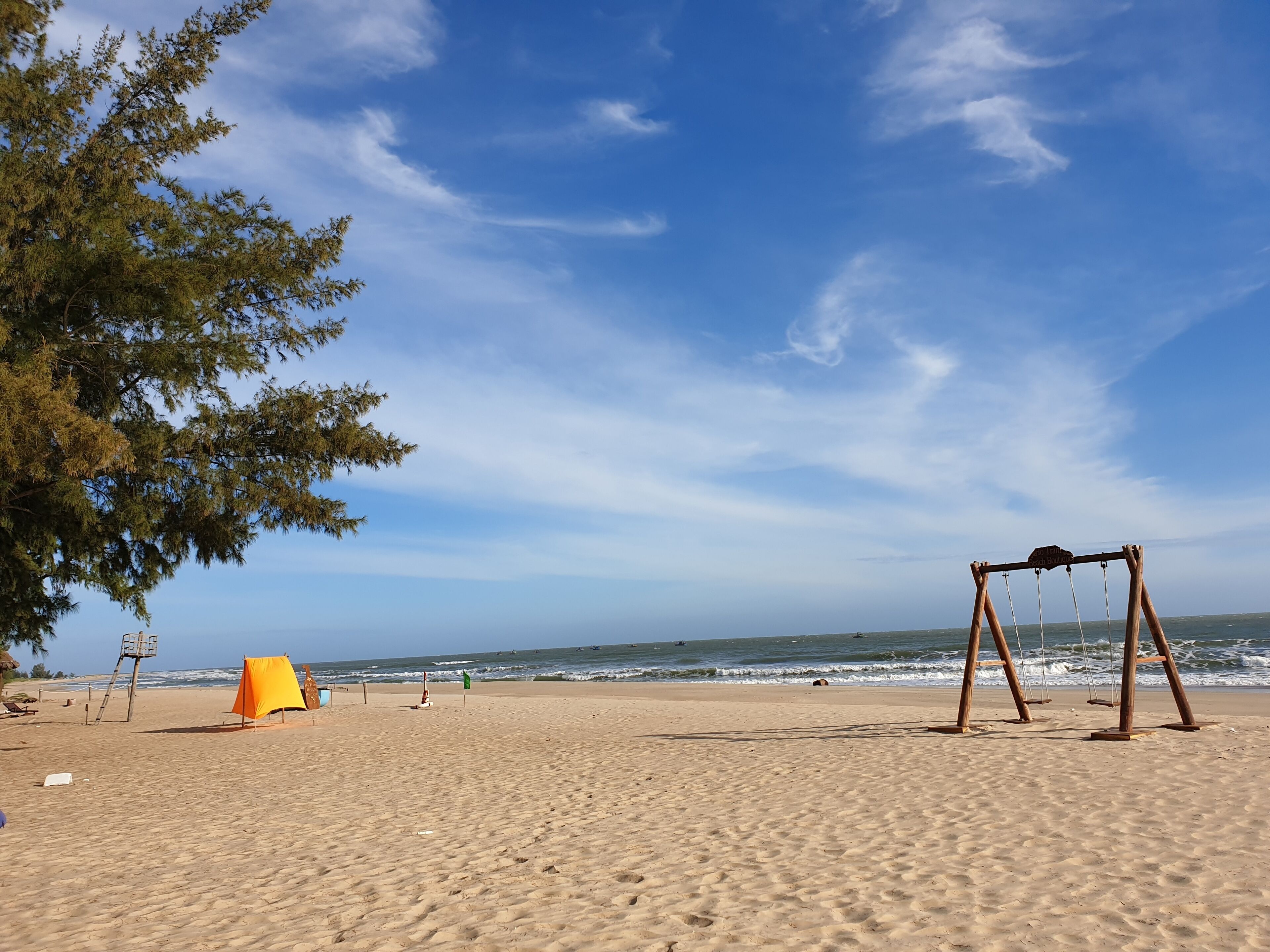 A beach with a swing set, a lifeguard tower, and a flag.