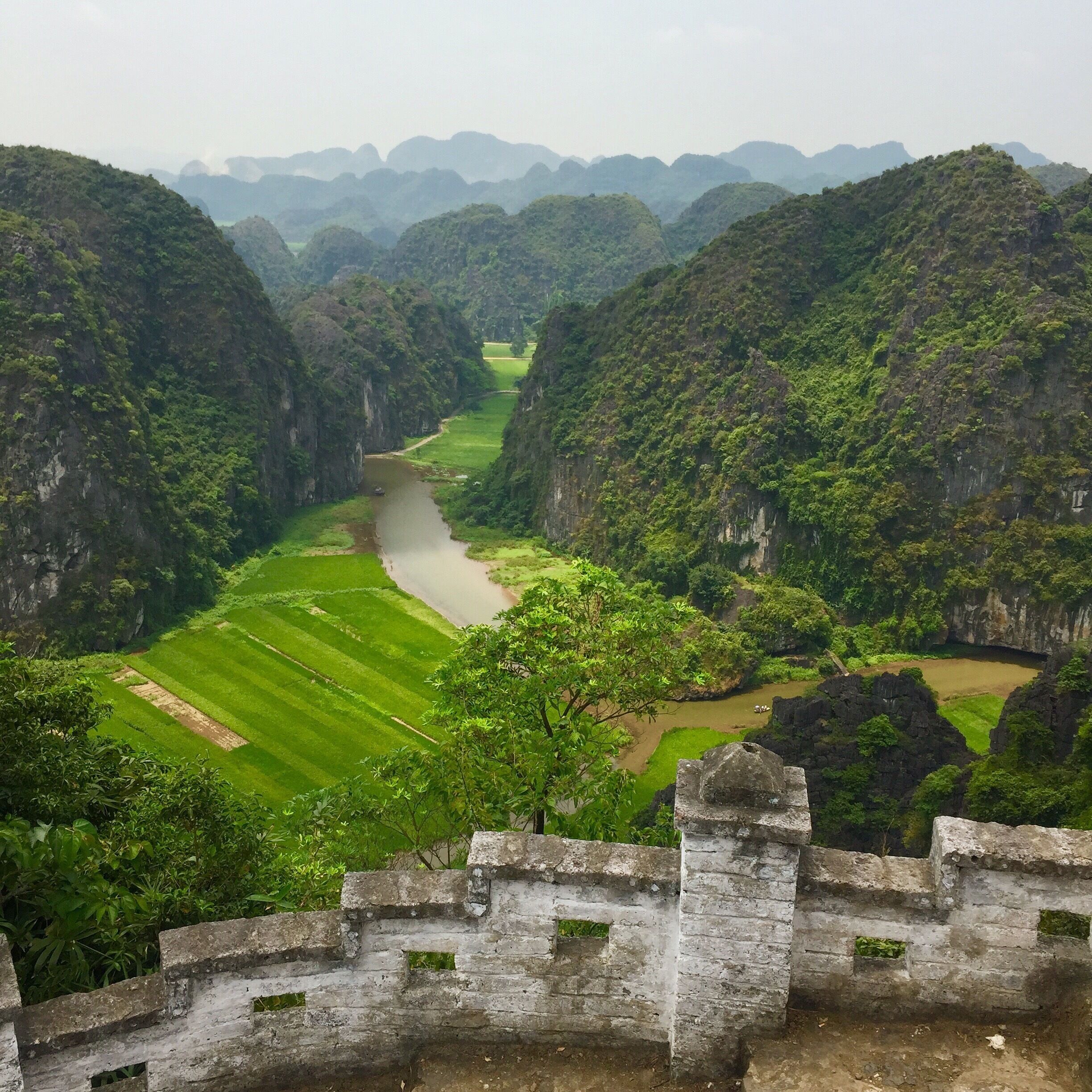 A river flowing through a valley with terraced fields and a stone wall in the foreground.