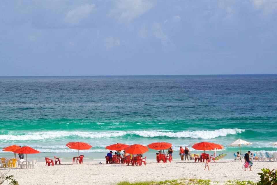 Uma praia com ondas azul-turquesa, guarda-sóis vermelhos e pessoas relaxando.
