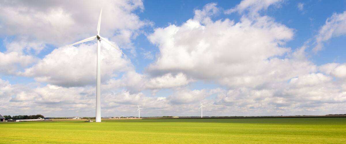 A wind farm with multiple wind turbines in a green field under a partly cloudy sky.