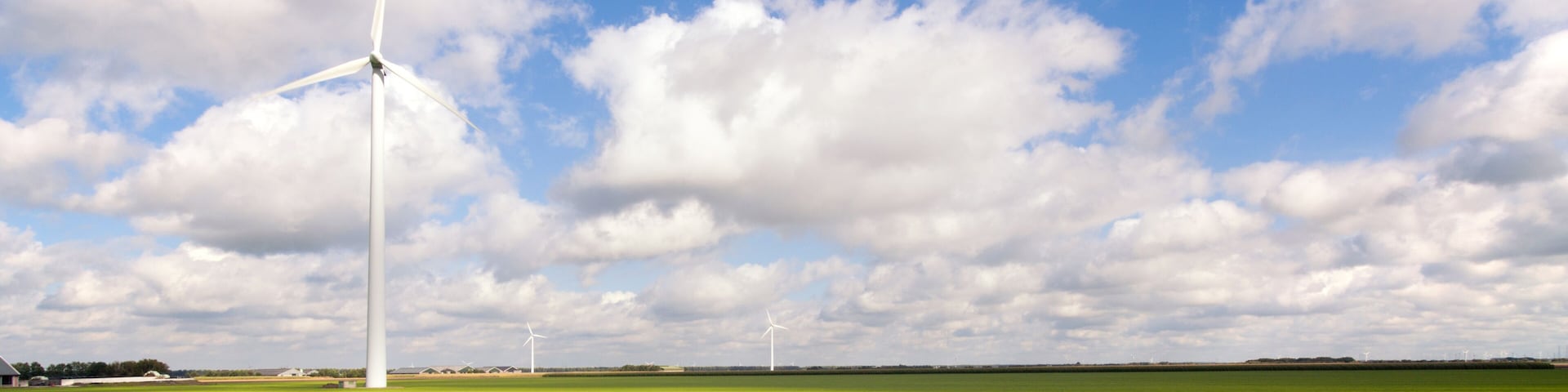 A wind farm with multiple wind turbines in a green field under a partly cloudy sky.