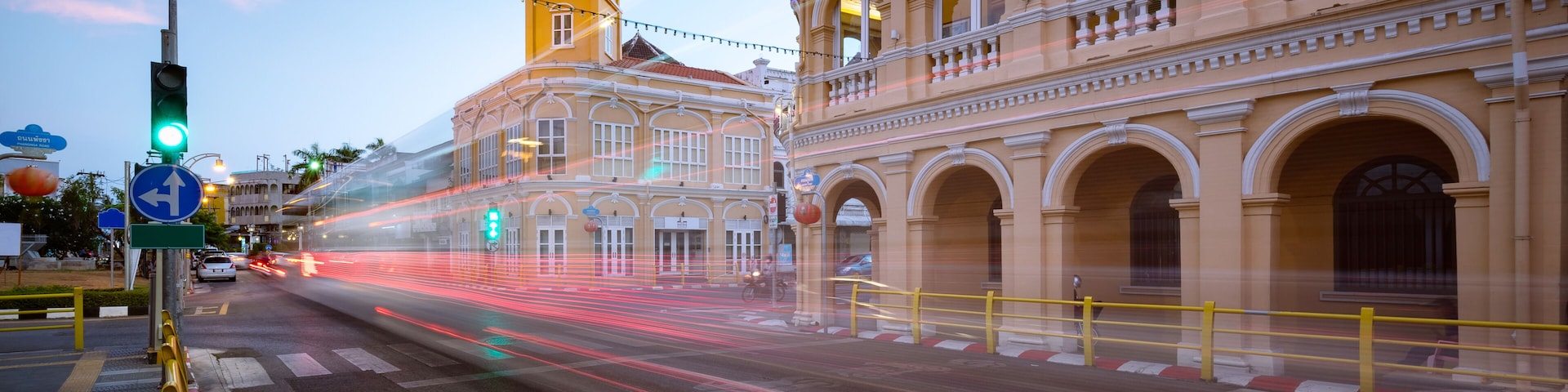 Um edifício histórico com torre de relógio, rua com semáforos e faixa de pedestres.