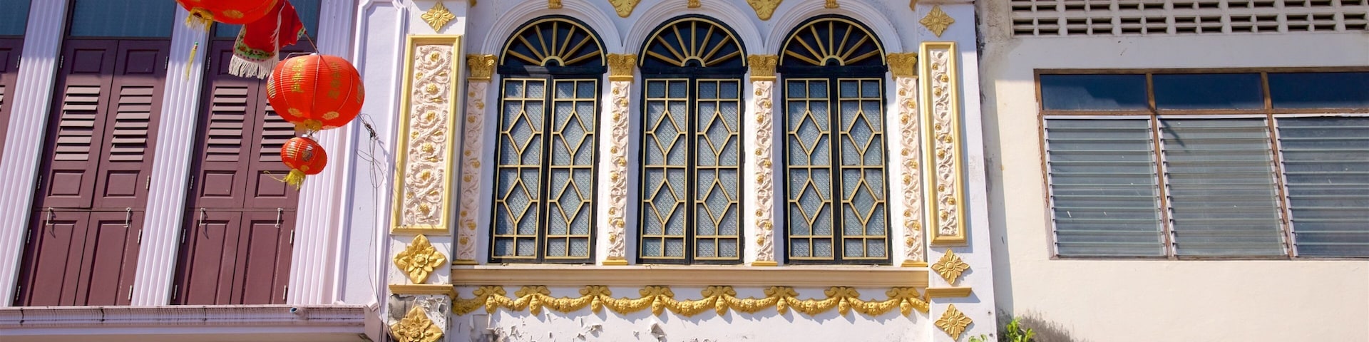 Um edifício com detalhes dourados ornamentados, janelas em arco grandes e lanternas vermelhas.