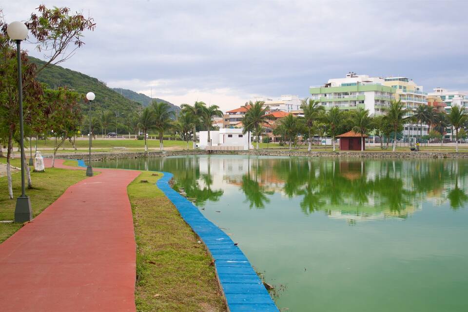Un parco con un sentiero rosso, una passerella blu e un lago tranquillo che riflette edifici e palme.