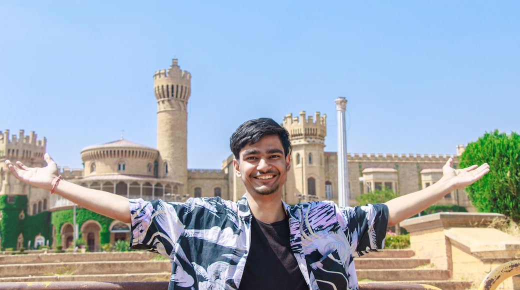 Una persona con le braccia aperte di fronte a un edificio storico con una torre e finestre ad arco.