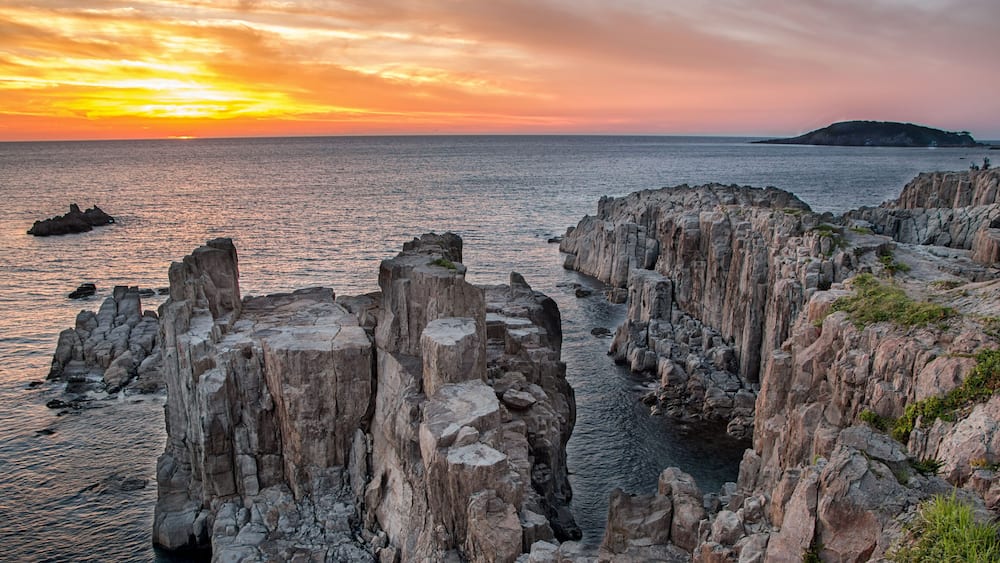 A coastal landscape with rocky cliffs and a sunset over the sea.