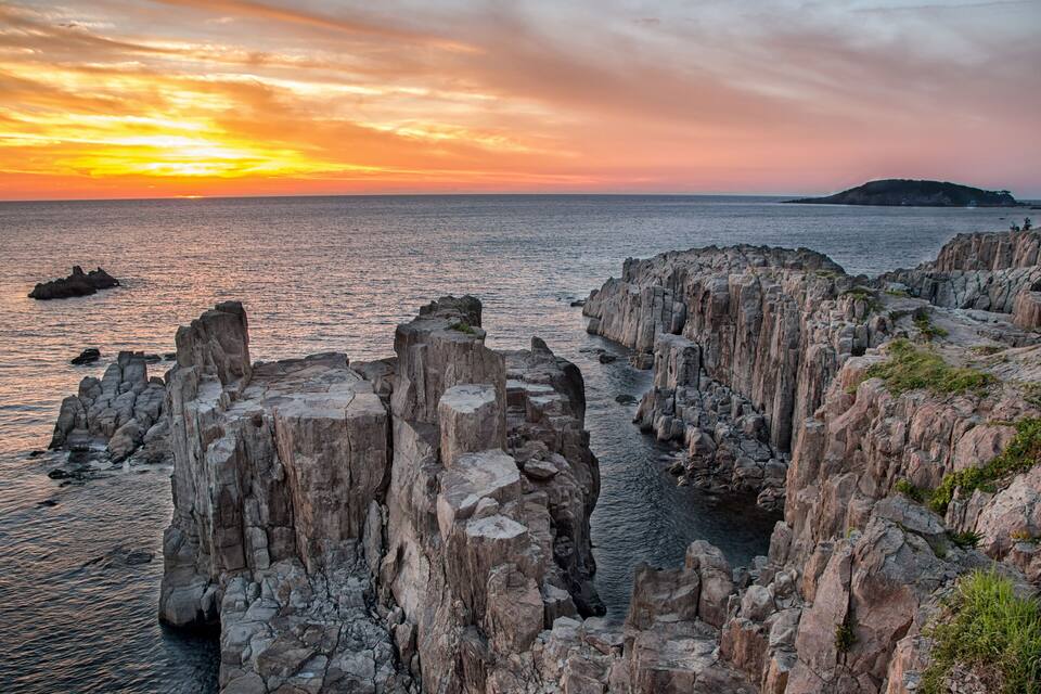 A coastal landscape with rocky cliffs and a sunset over the sea.