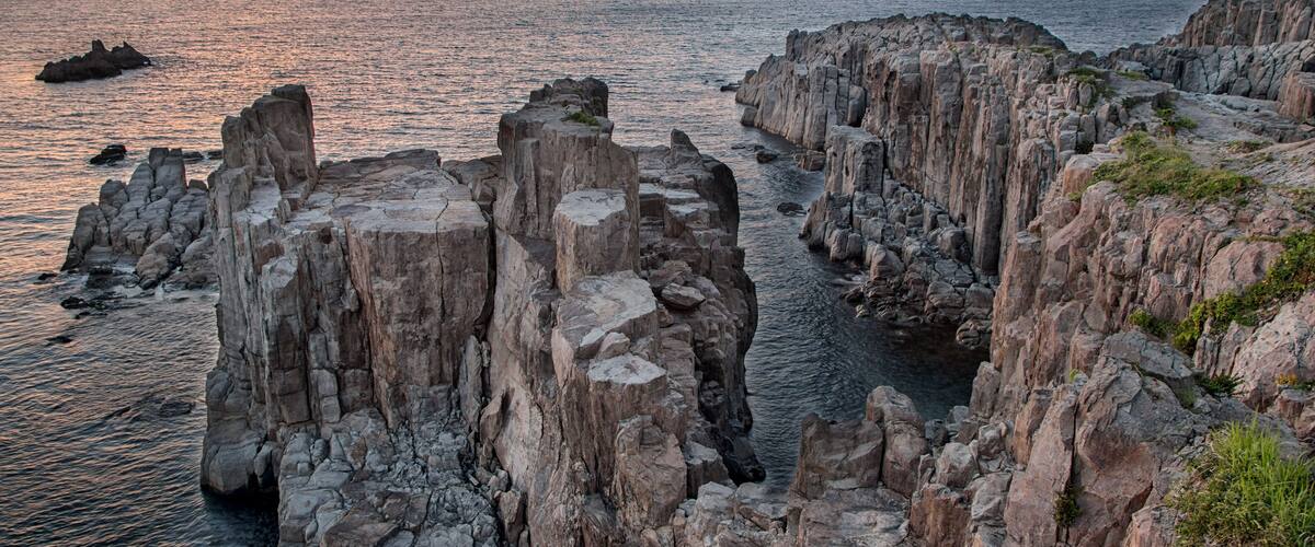 A coastal landscape with rocky cliffs and a sunset over the sea.