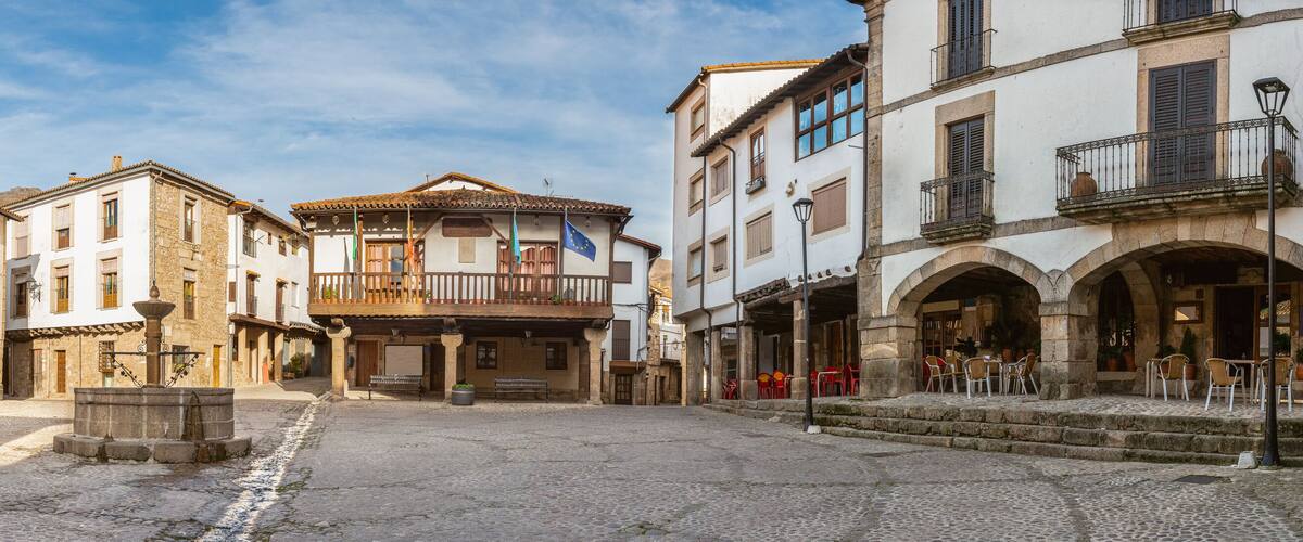A cobblestone street in a historic town with old buildings, a fountain, and outdoor seating.