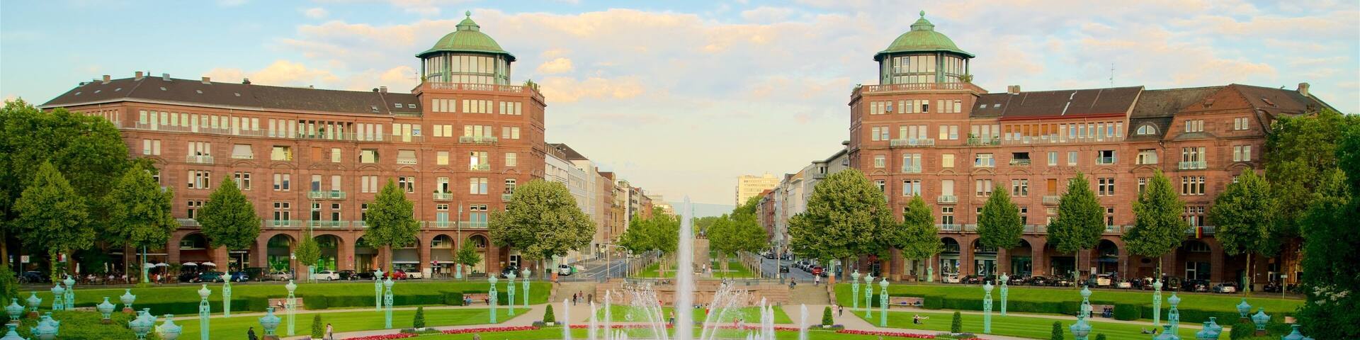 A grand fountain in the center of a well-manicured square, surrounded by symmetrical buildings and lush greenery.