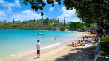 A beach with clear turquoise water, people sunbathing and swimming, and buildings in the background.