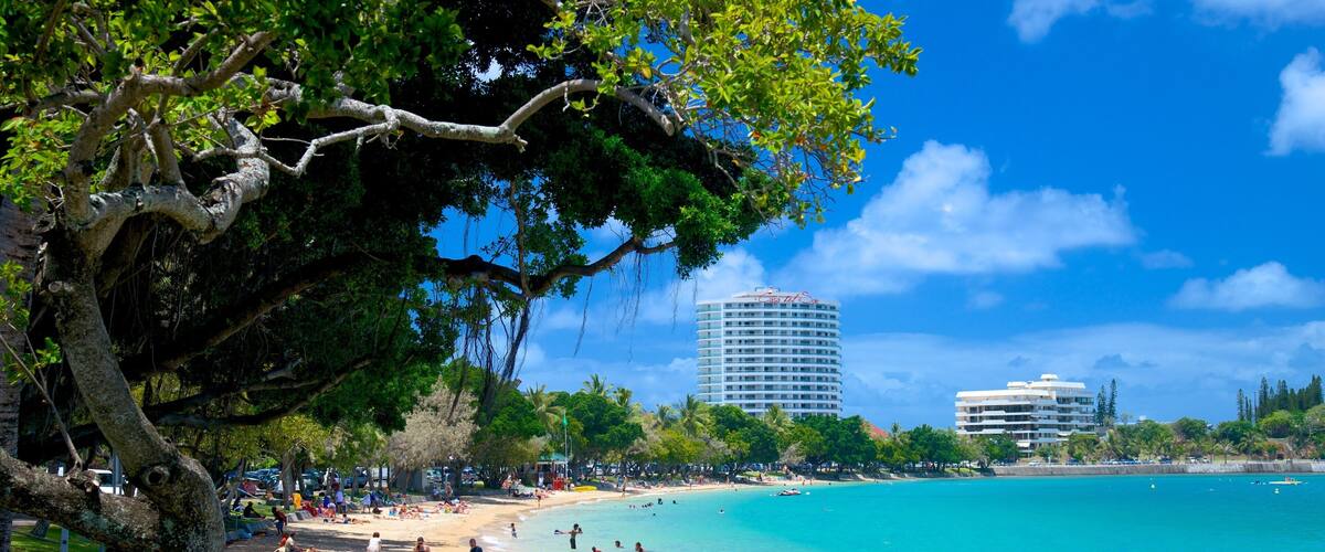 A beach with clear turquoise water, people sunbathing, and tall buildings in the background.