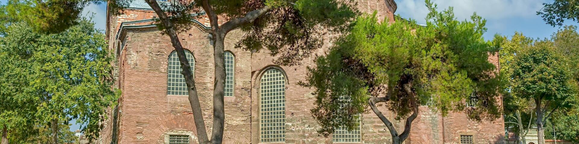 A historic building with a dome and arched windows, surrounded by trees and a grassy area.