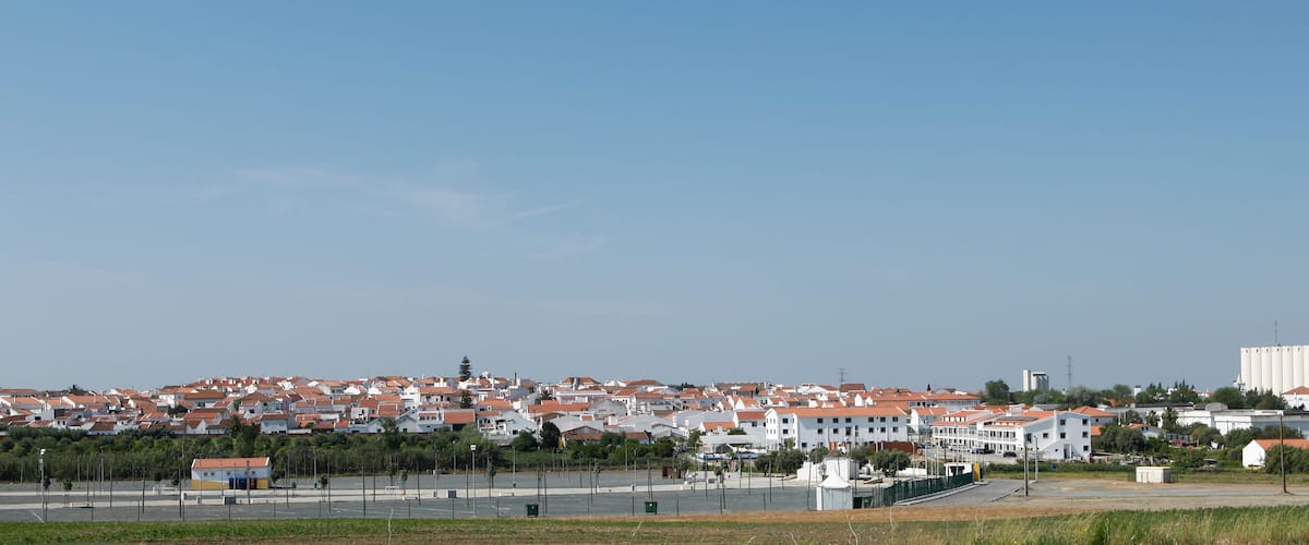 A coastal town with red-roofed houses, a large grain silo, and a clear blue sky.