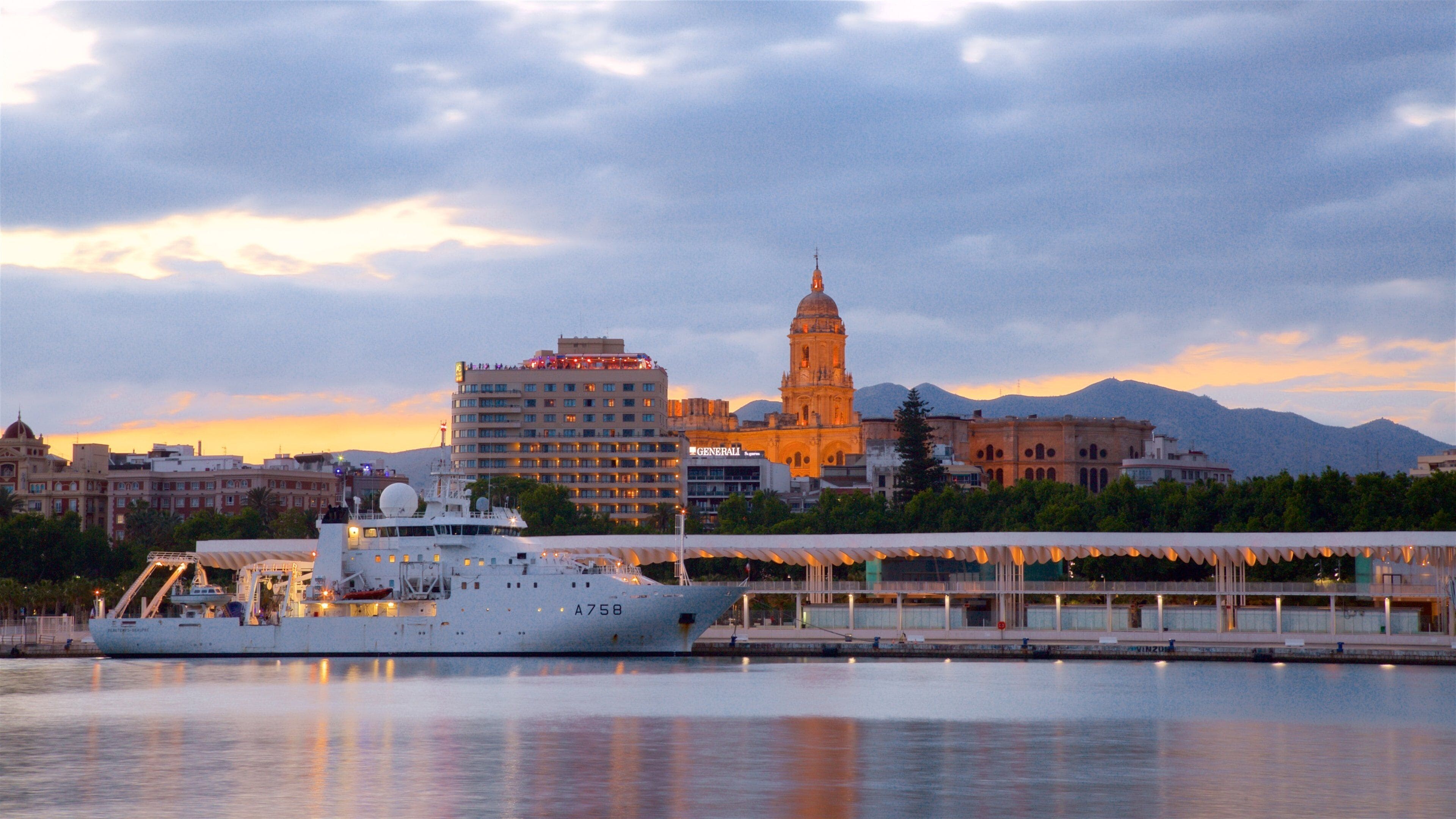 Ein großes Schiff liegt an einem Hafen vor einer Stadtlandschaft, darunter ein markantes Gebäude mit einer Kuppel.