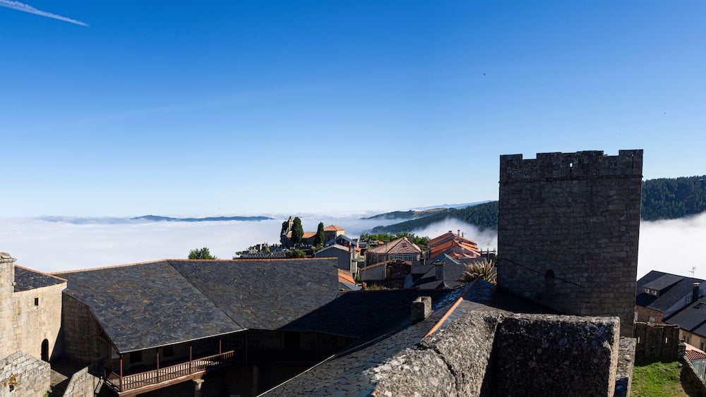 Pueblo Bonito de España, Castro Caldelas, Orense, verano de 2021, vista panorámica desde el castillo medieval, de los tejados, torre y campanario sobre fondo de nubes blanco y cielo azul.