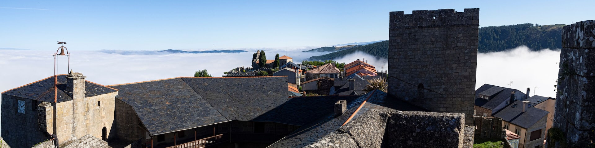 Pueblo Bonito de España, Castro Caldelas, Orense, verano de 2021, vista panorámica desde el castillo medieval, de los tejados, torre y campanario sobre fondo de nubes blanco y cielo azul.