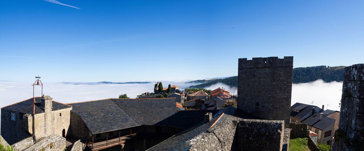 A historic town with stone buildings, a prominent tower, and a view of mist-covered mountains.
