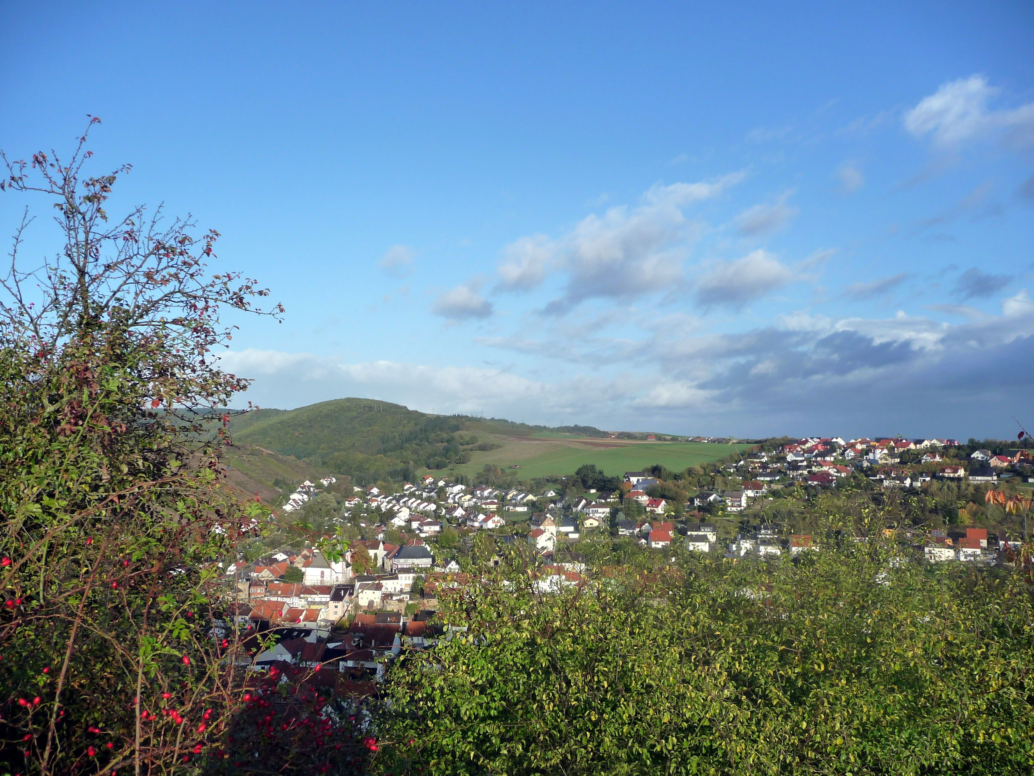 A village nestled in a valley with green hills in the background.