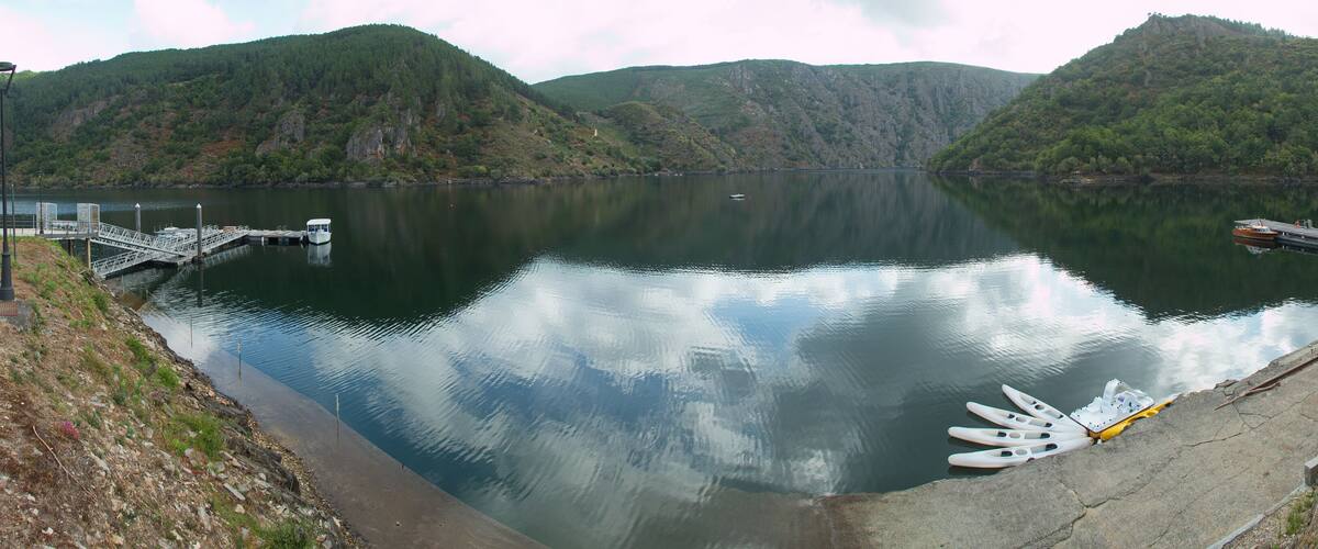 A calm lake with boats docked at a pier, surrounded by lush green hills.