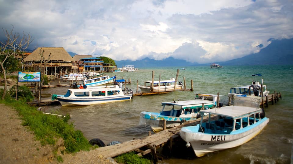 A coastal village with boats docked at wooden piers, surrounded by lush greenery and a mountain range in the background.