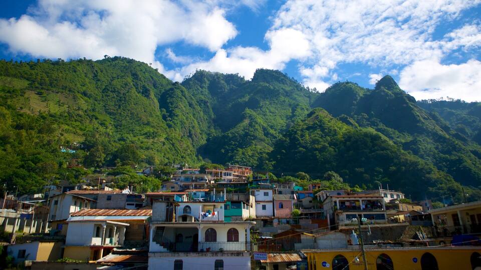 A hillside town with colorful buildings nestled against lush green mountains under a partly cloudy sky.