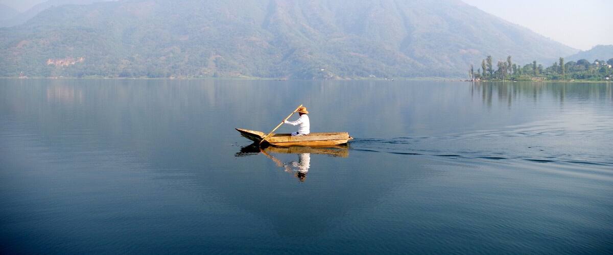 A person rowing a boat on a calm lake with a mountain in the background.