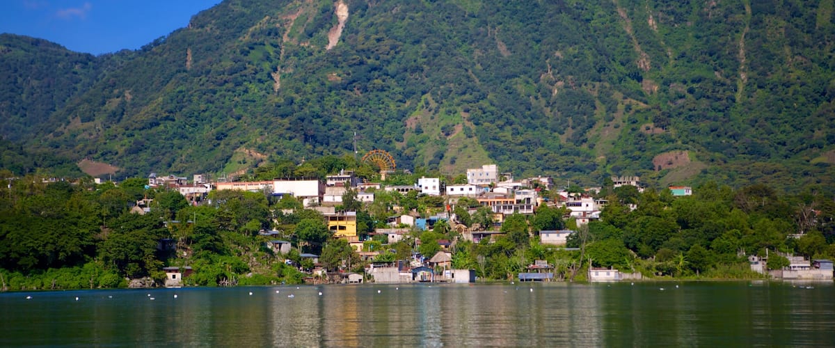 A lakeside town with a Ferris wheel, surrounded by lush green hills.