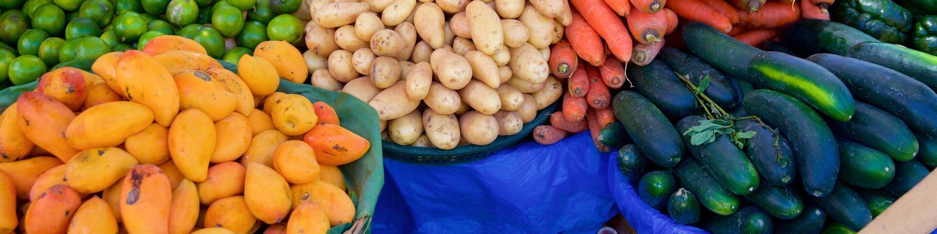 Variedad de verduras frescas, incluyendo papas, zanahorias y pepinos, exhibidas en un mercado.