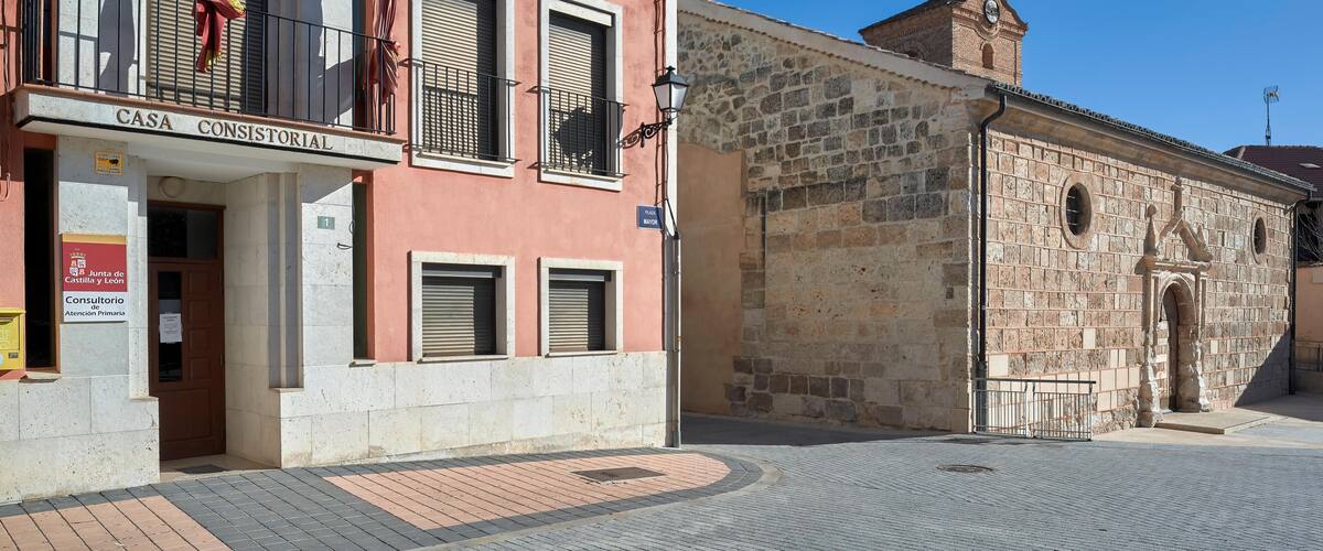 A building labeled "CASA CONSISTORIAL" with a stone wall and a clock tower in the background.