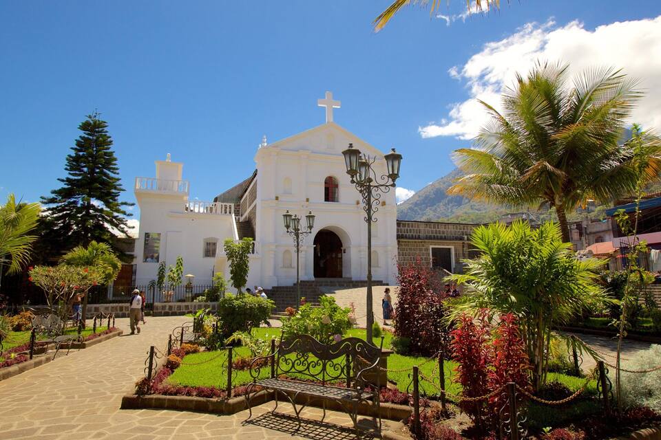 A white church with a cross on top, surrounded by tropical plants and a clear blue sky.