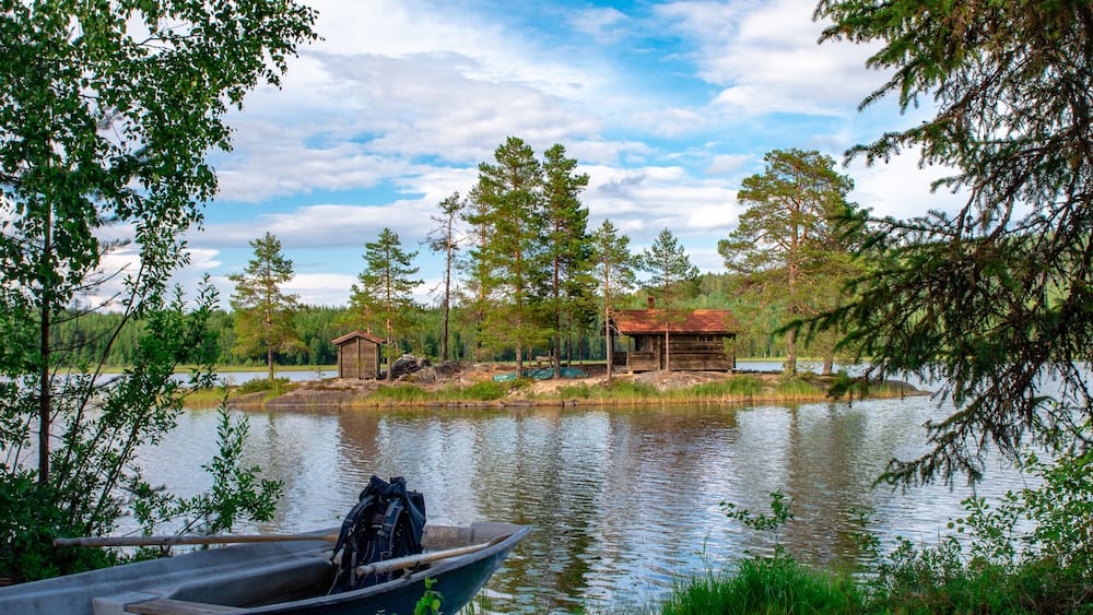 Ein Haus auf einer Insel eines schwedischen Sees im Hälsingland. Davor ein Boot mit einem Rucksack.