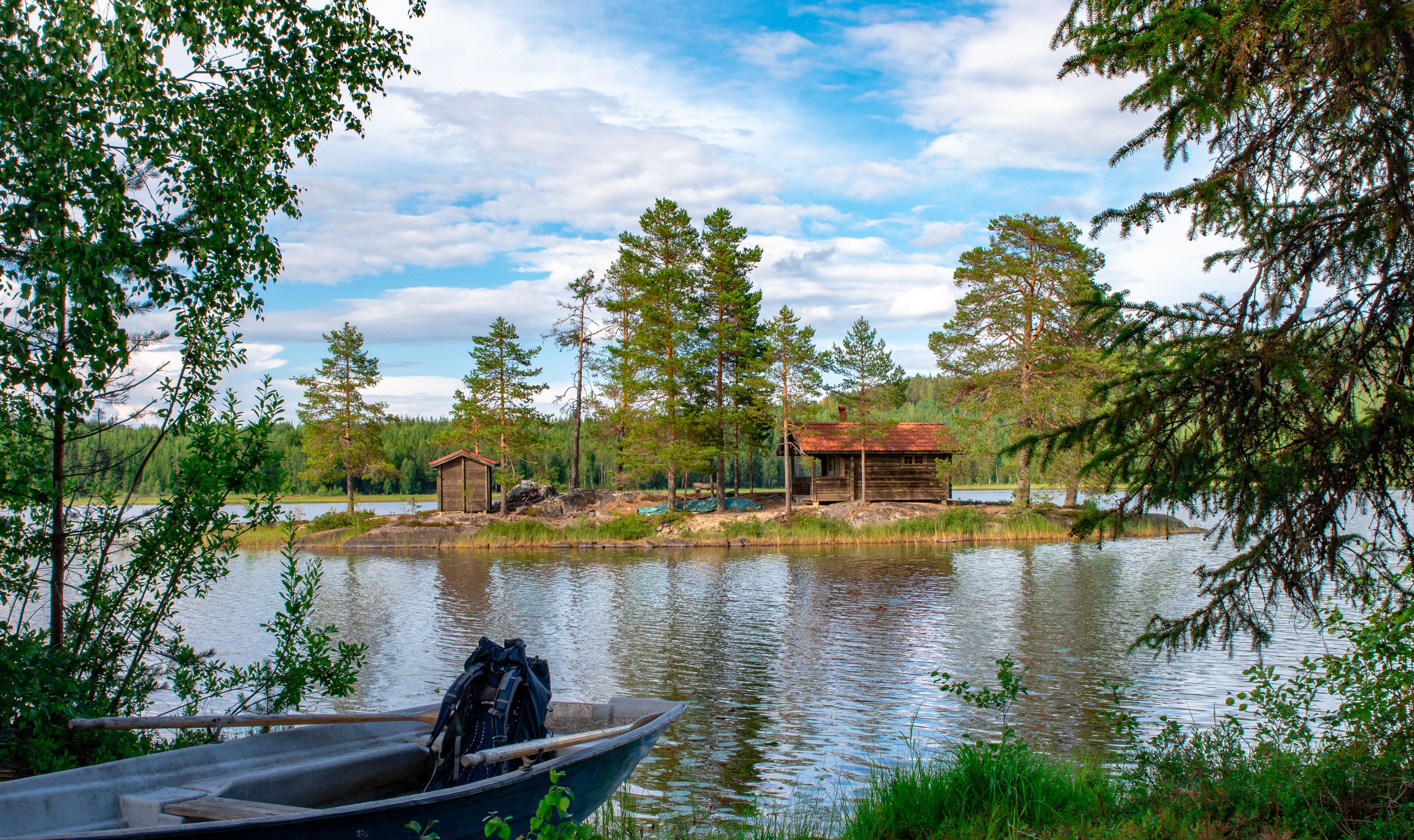 A calm lake with a wooden cabin and a boat docked near the shore.