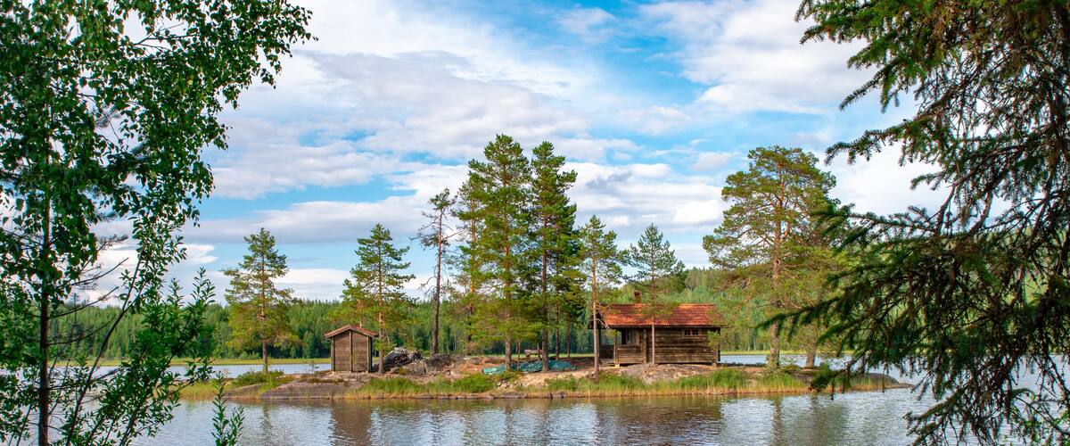 A calm lake with a wooden cabin and a boat docked near the shore.