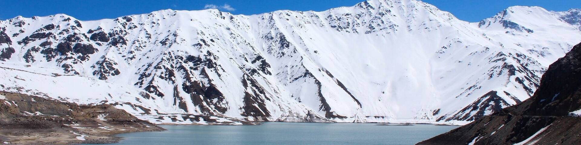 A snow-covered mountain range with a calm blue lake in the foreground.