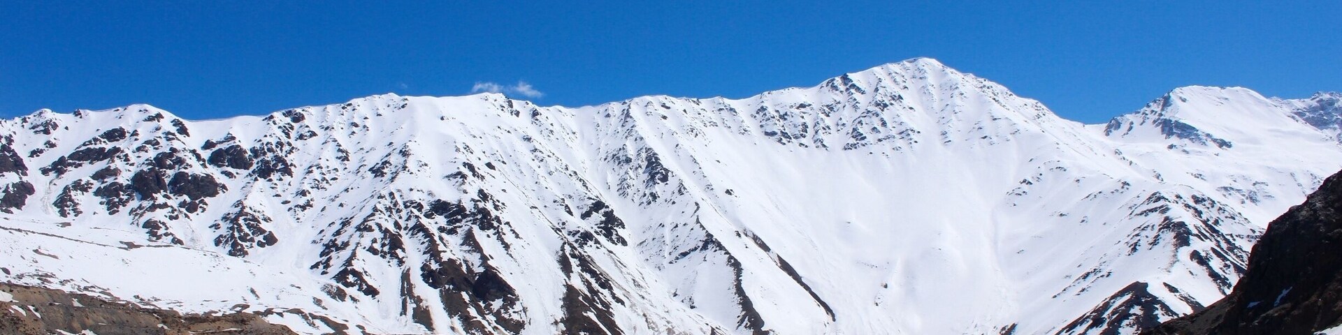 Una cordillera nevada con un lago azul tranquilo al frente.