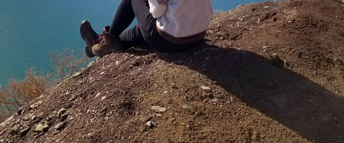 A woman sitting by a lake with snow-capped mountains in the background.