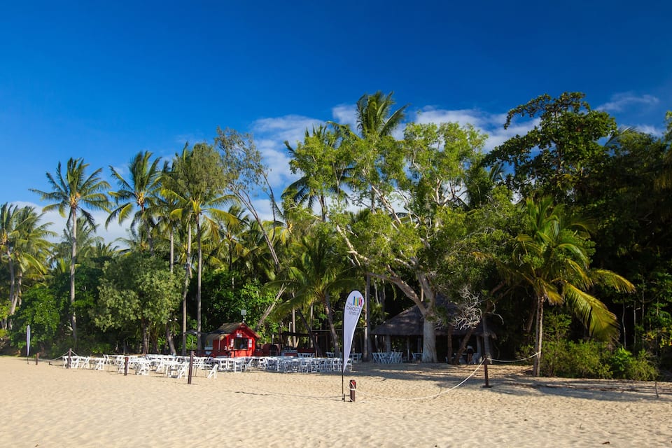 Ein Strand mit Palmen, einer roten Struktur und weißen Stühlen, die für eine Veranstaltung aufgestellt sind.