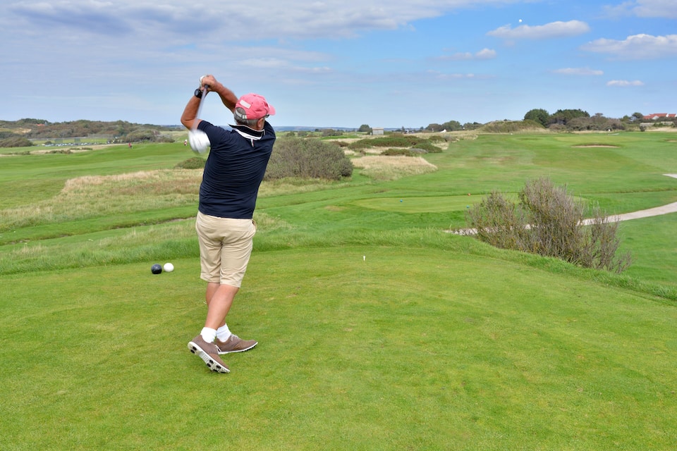 A golf course with a golfer in mid-swing, a golf ball, and a clear sky.