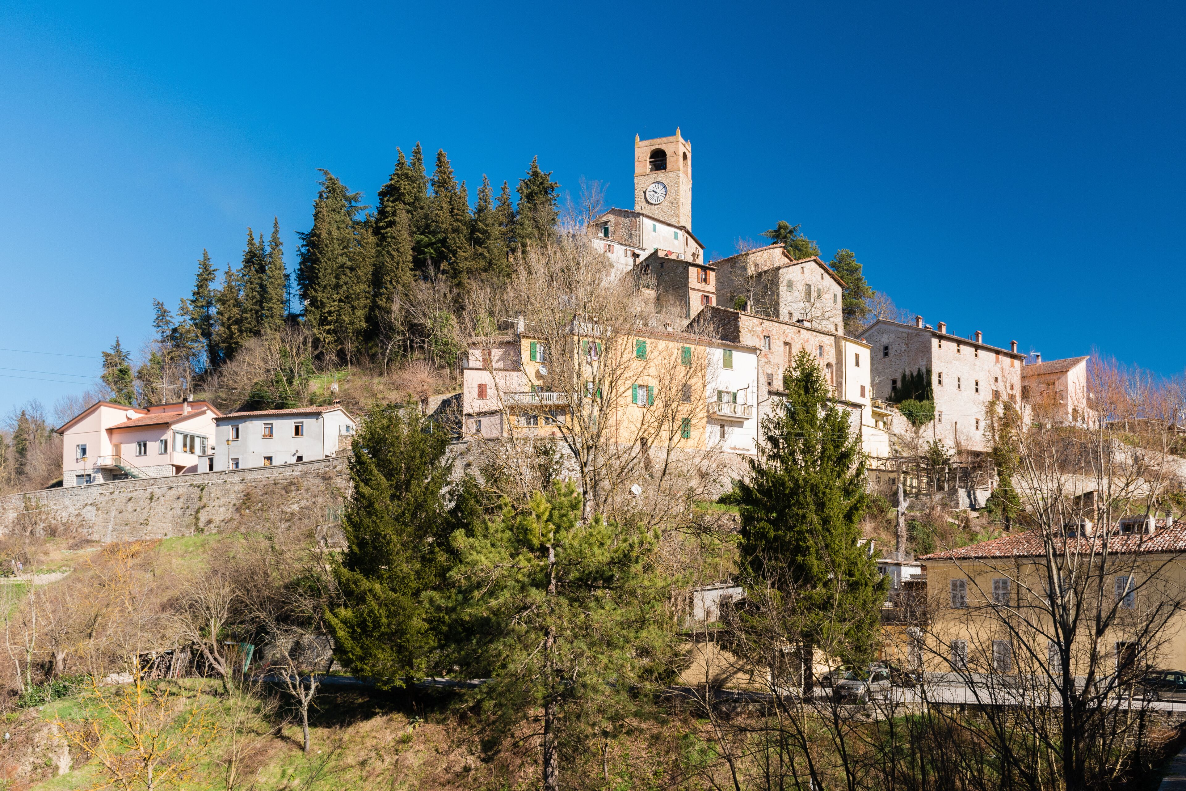 A historic town with a prominent clock tower on a hill, surrounded by trees and buildings.