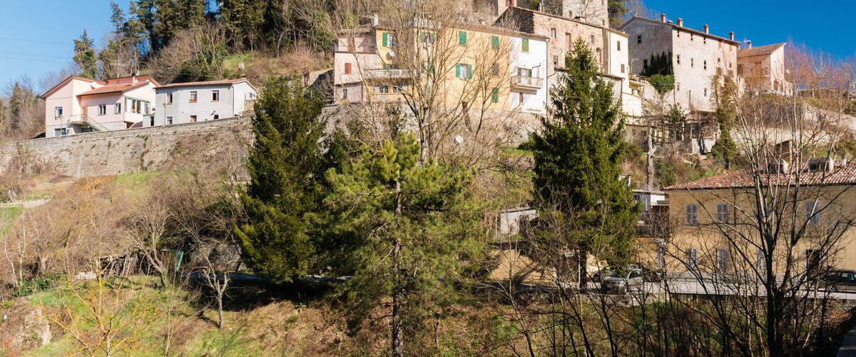 A historic town with a prominent clock tower on a hill, surrounded by trees and buildings.