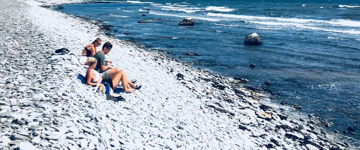 A beach with people sitting on the shore, waves crashing, and a clear blue sky.