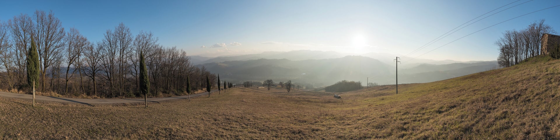 A rural landscape with a road, trees, and distant mountains under a clear sky.