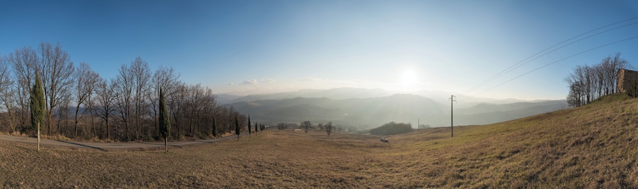 A rural landscape with a road, trees, and distant mountains under a clear sky.
