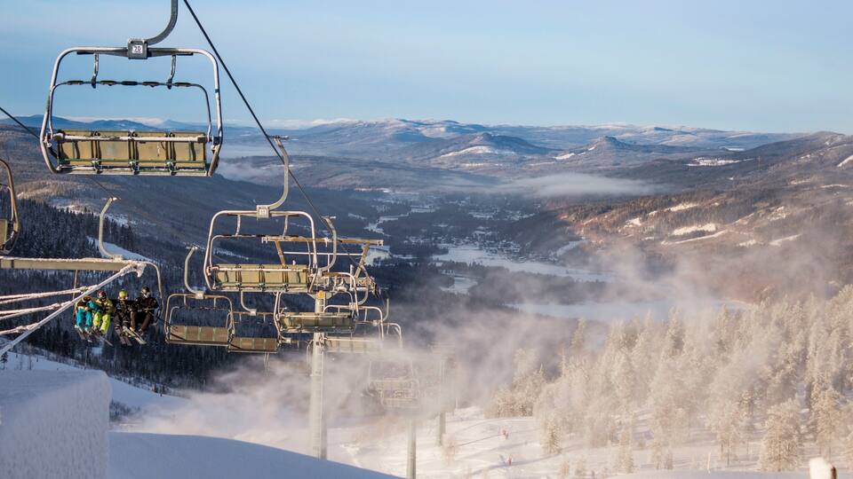 A ski lift with passengers, snow-covered trees, and a mountainous landscape.
