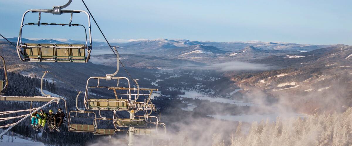 A ski lift with passengers, snow-covered trees, and a mountainous landscape.