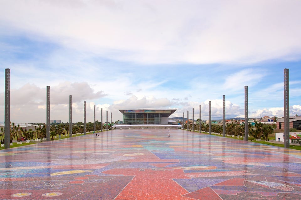 Une place dallée de motifs colorés qui mène à un bâtiment moderne doté d’une façade en verre.