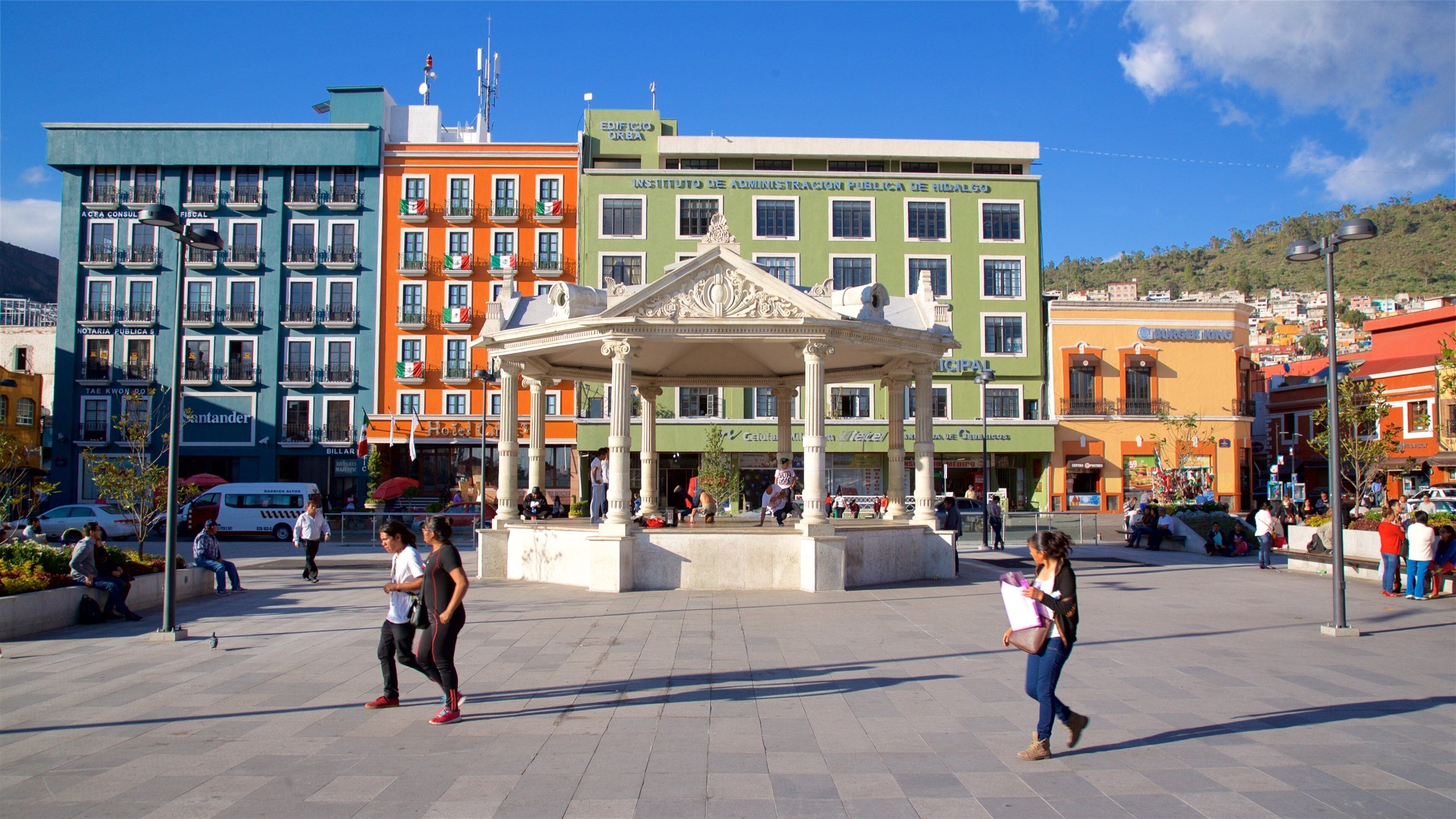 A plaza with a central gazebo, surrounded by colorful buildings, including a green building labeled "Instituto de Administracion Publica de Hidalgo".