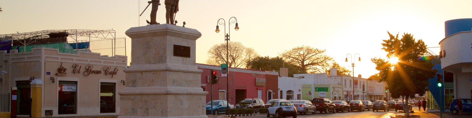 Una estatua en una plaza, con edificios circundantes y coches aparcados.