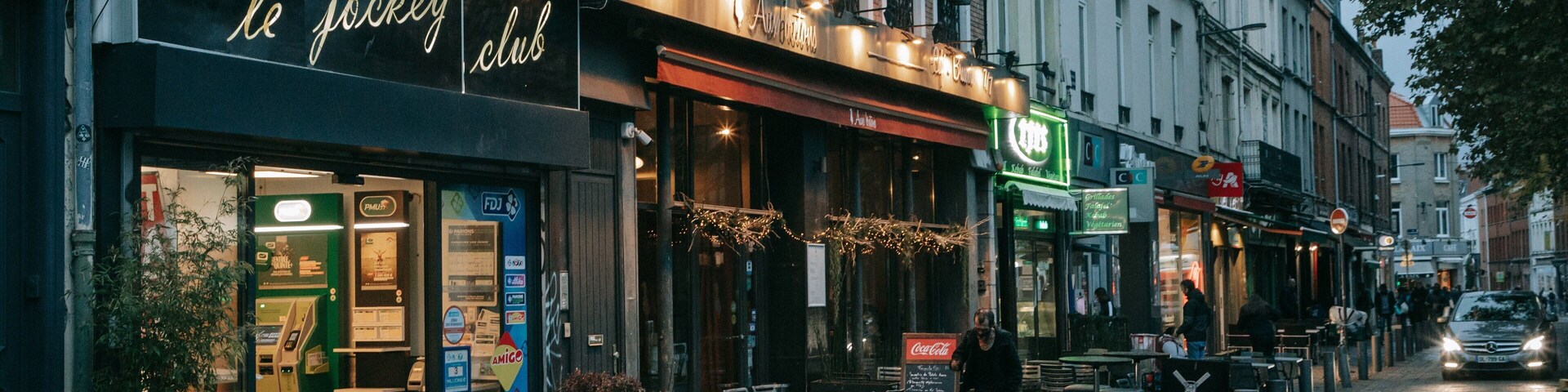 Una calle empedrada bordeada de cafés y tiendas, incluyendo 'le jockey club' y 'Cafe du Monde'.
